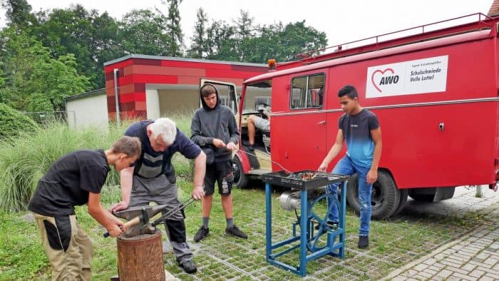 Justin (von rechts), Fabian und Nick werden von Lehrer Michael Werner beim Schmieden angeleitet. Auch externe Schulen können die stationäre Schmiede und das Schmiedemobil nutzen. Foto: Stefan Lohmann / regios24