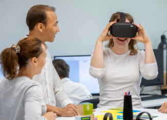 Drei Personen im Basement des Georg-Eckert-Instituts, eine davin trägt lächelnd eine VR-Brille.