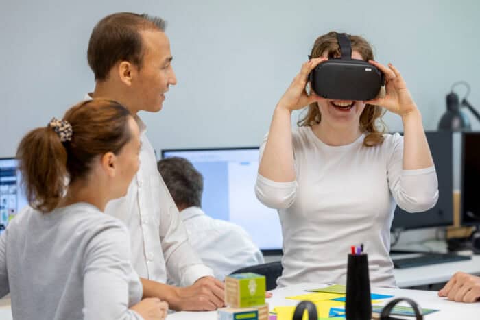 Drei Personen im Basement des Georg-Eckert-Instituts, eine davin trägt lächelnd eine VR-Brille.