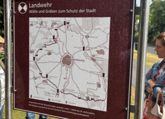 Die Frontseite des neuen BLIK-Schildes am Lammer Holz zeigt den Verlauf des Landwehrs. Links im Bild Rudolf Rischmann von der Schwabe-Stiftung Kuchelberg, rechts Sabrina Brandes, Ortsheimatpflegerin Lehndorf. Foto: Stadtheimatpflege